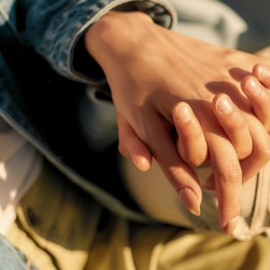 Close up of hands of lesbian couple. Two girls holding their hands, sitting on the bench on a sunny day, spending time together outdoors. Homosexuality, LGBT, love. Selective focus. Horizontal shot